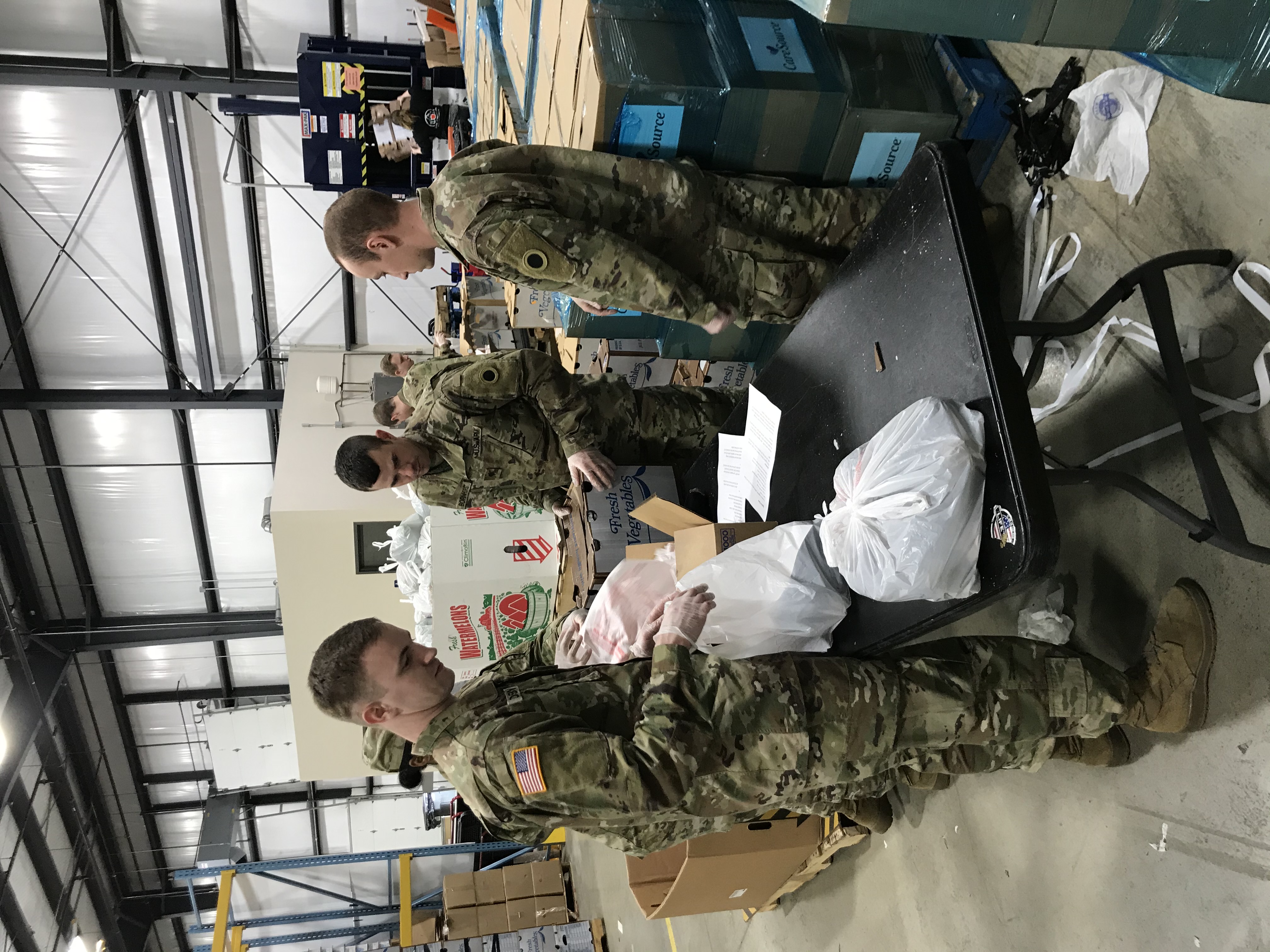 Soldiers pack fresh vegetables into bags inside warehouse.