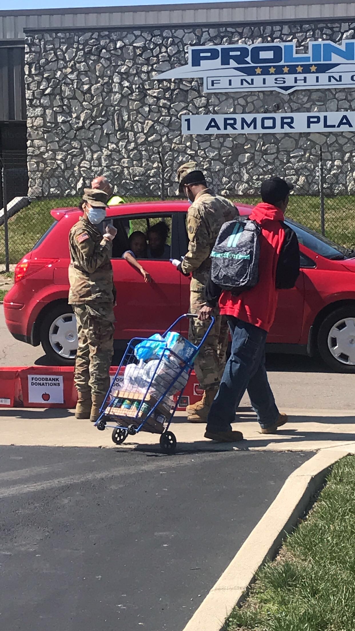 Soldiers hand supplies to cars curbside.